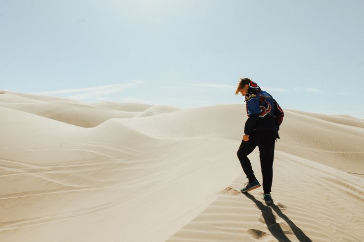 a person with a backpack is walking in the sand dunes, looking up at the sky