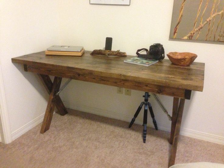 a wooden table sitting next to a wall with pictures on the wall above it and a camera