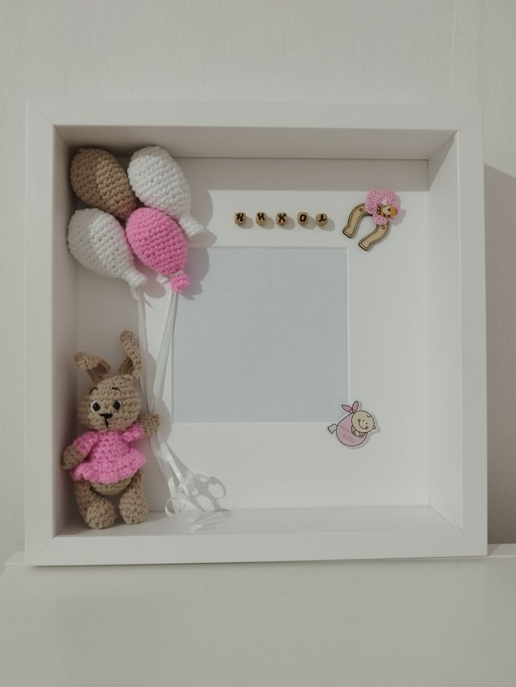 a teddy bear is sitting in front of a white frame with pink decorations on it