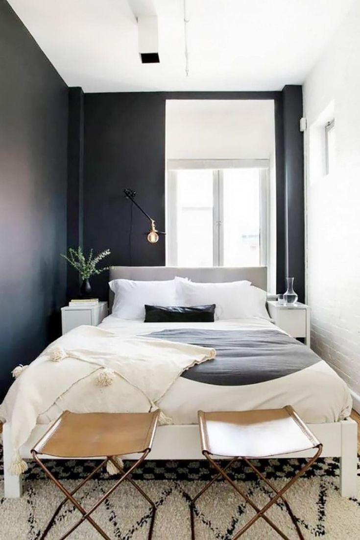 a bedroom with black walls, white bedding and two chairs in front of the bed