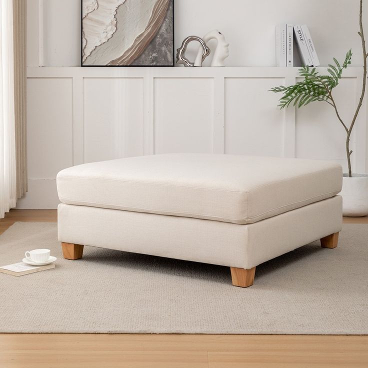 a white ottoman sitting on top of a wooden floor next to a plant in a vase