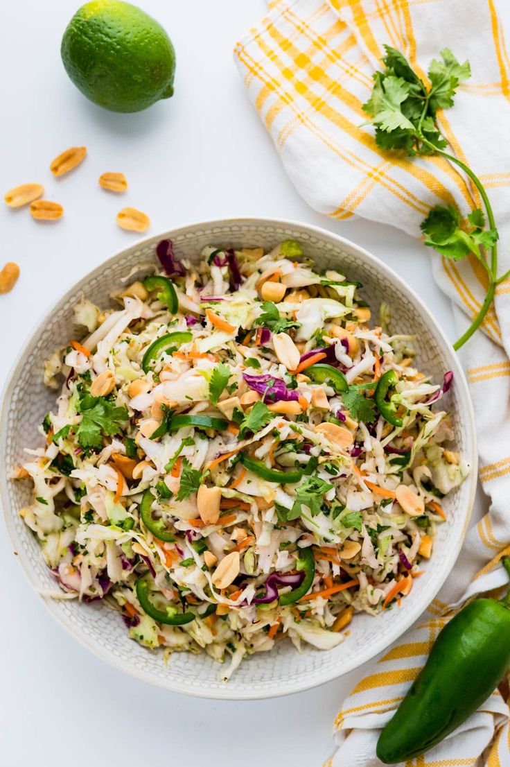 a white bowl filled with coleslaw slaw next to limes and peanuts