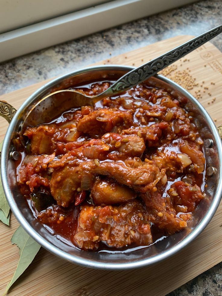 a bowl filled with meat and sauce on top of a cutting board next to a knife