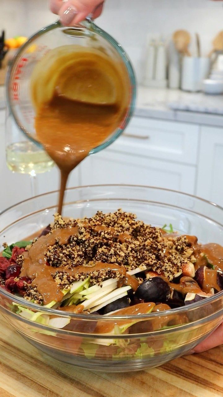 someone pouring dressing over a salad in a glass bowl on top of a wooden table