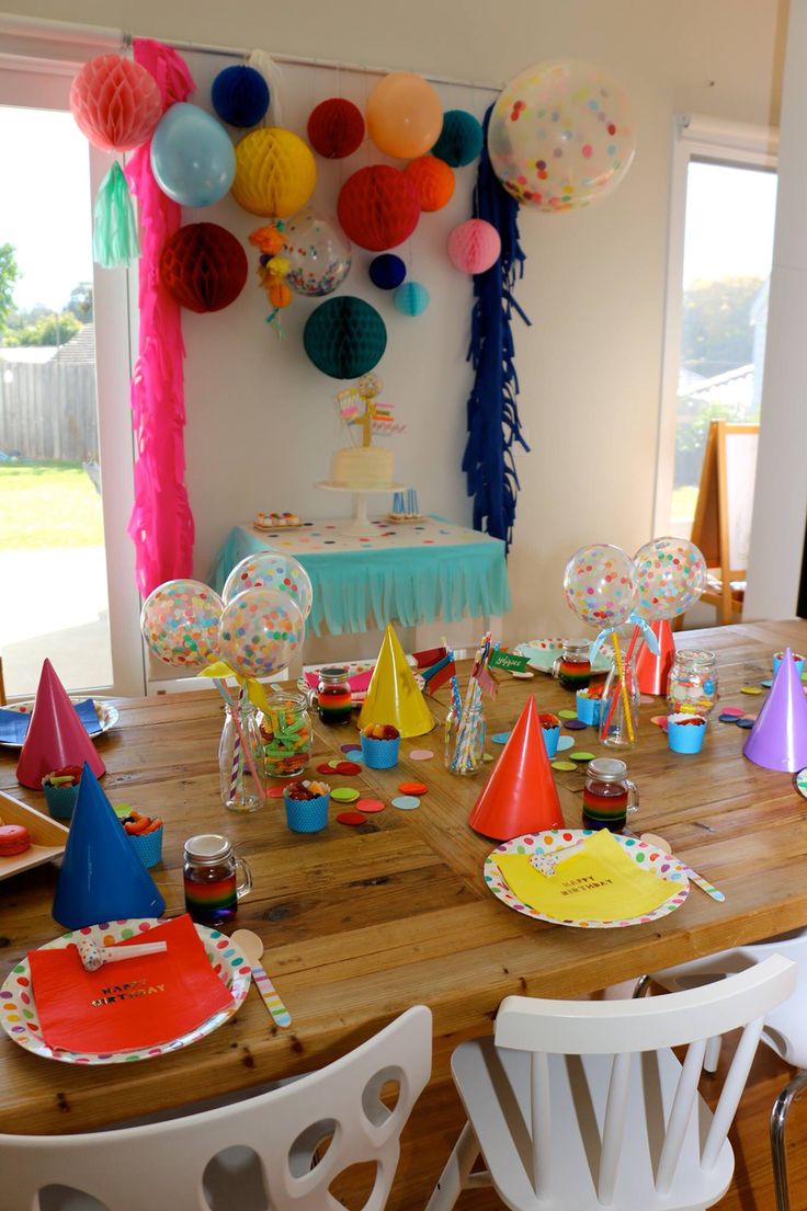 a party table set up with balloons, paper hats and streamers on the wall