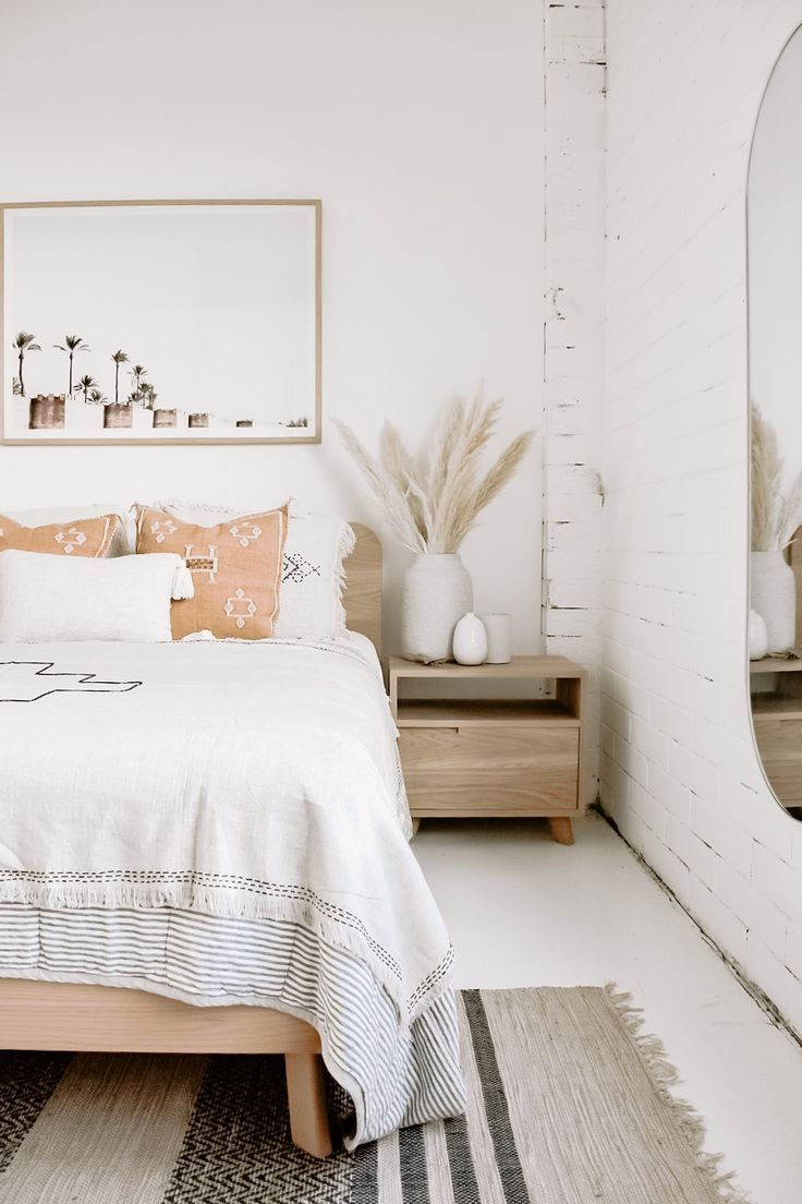 a bedroom with white walls and wooden furniture, including a large mirror above the bed