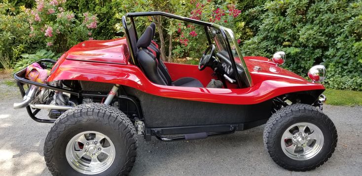 a red dune buggy is parked in front of some bushes