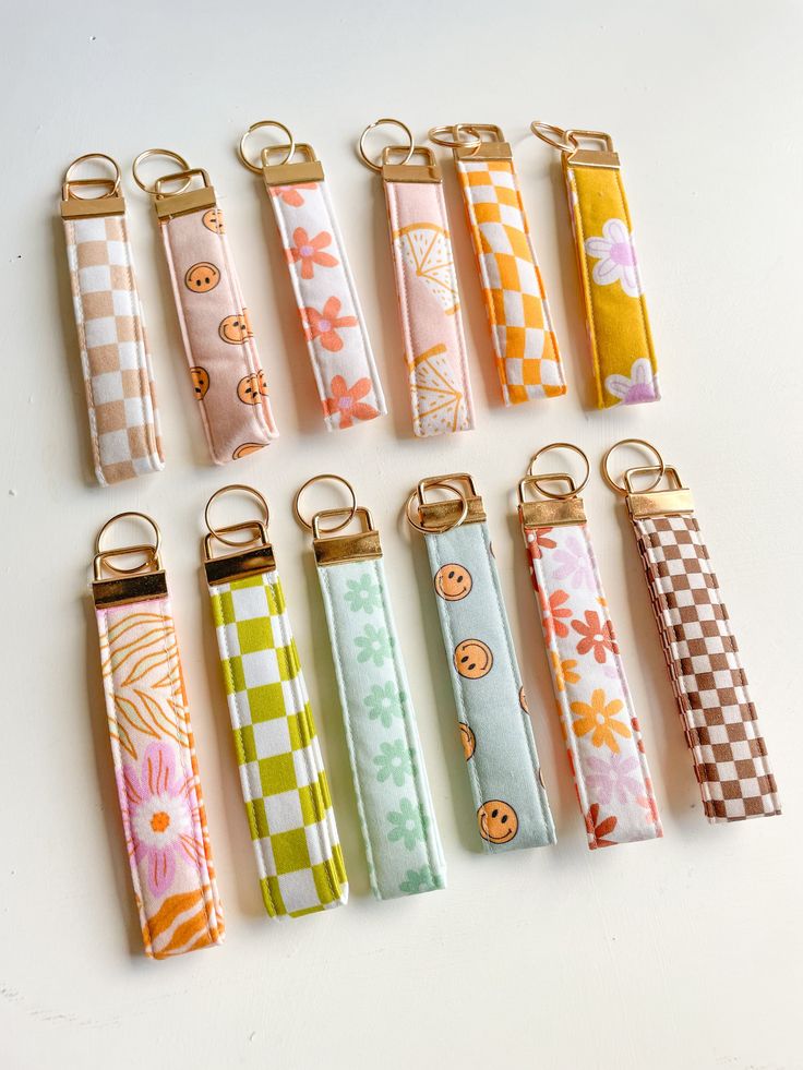 eight different colored keychains are lined up on a white surface, each with an individual's name