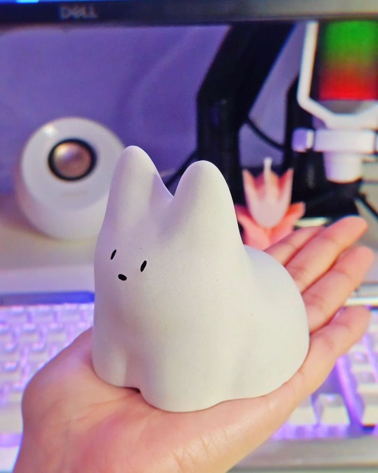 a hand holding a small white ghost figurine in front of a computer keyboard