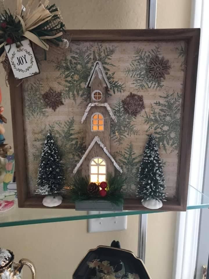 a christmas scene is displayed on a shelf in front of a window with snowflakes and evergreens