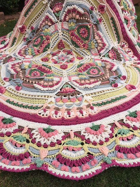 a crocheted blanket sitting on top of grass covered in pink and green yarn