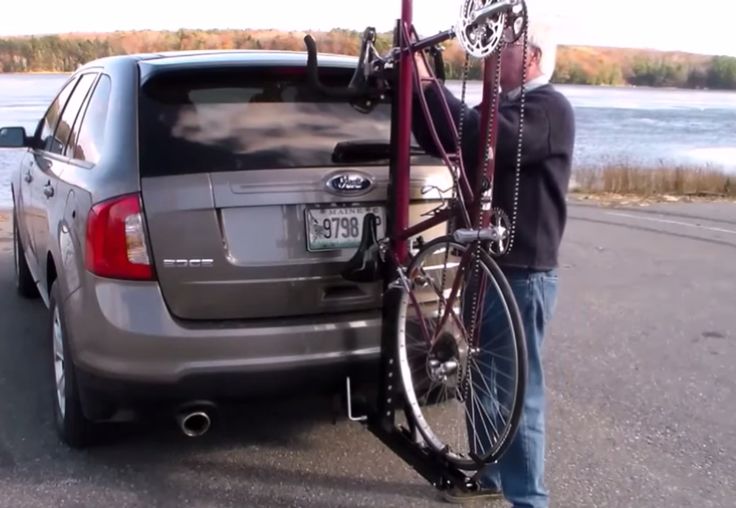 a man standing next to a car with a bike on it's back rack