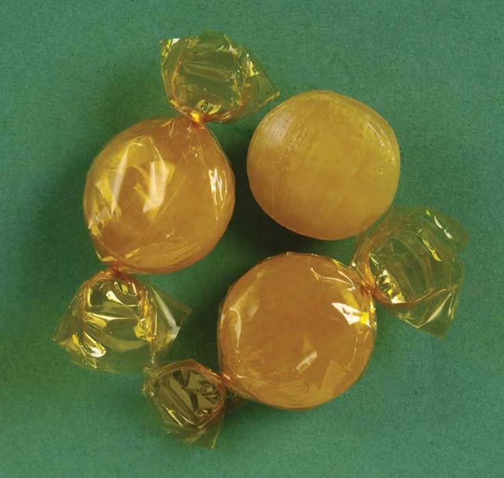 four pieces of yellow candy sitting on top of a green tableclothed surface with gold foil wrapped around them