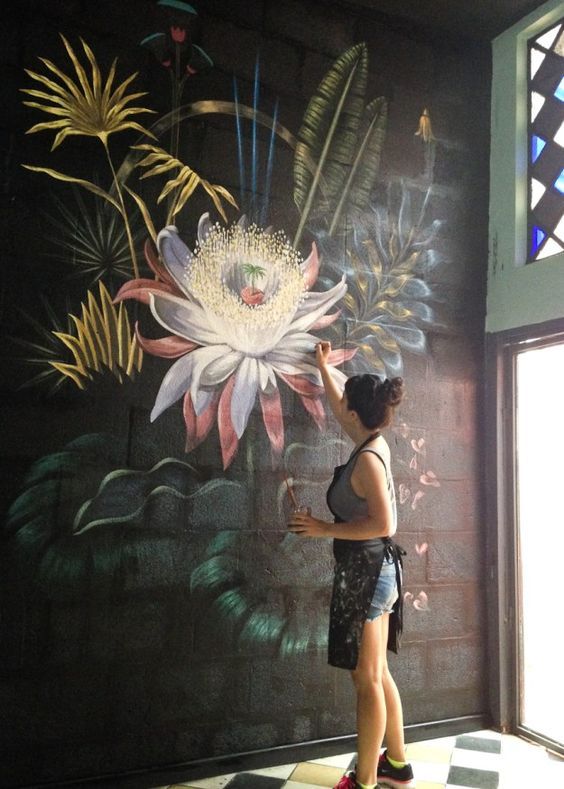 a woman standing in front of a wall with flowers painted on it's side