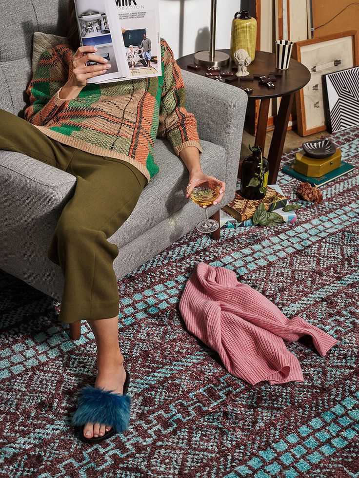 a woman is sitting on a couch reading a magazine and holding a glass of wine