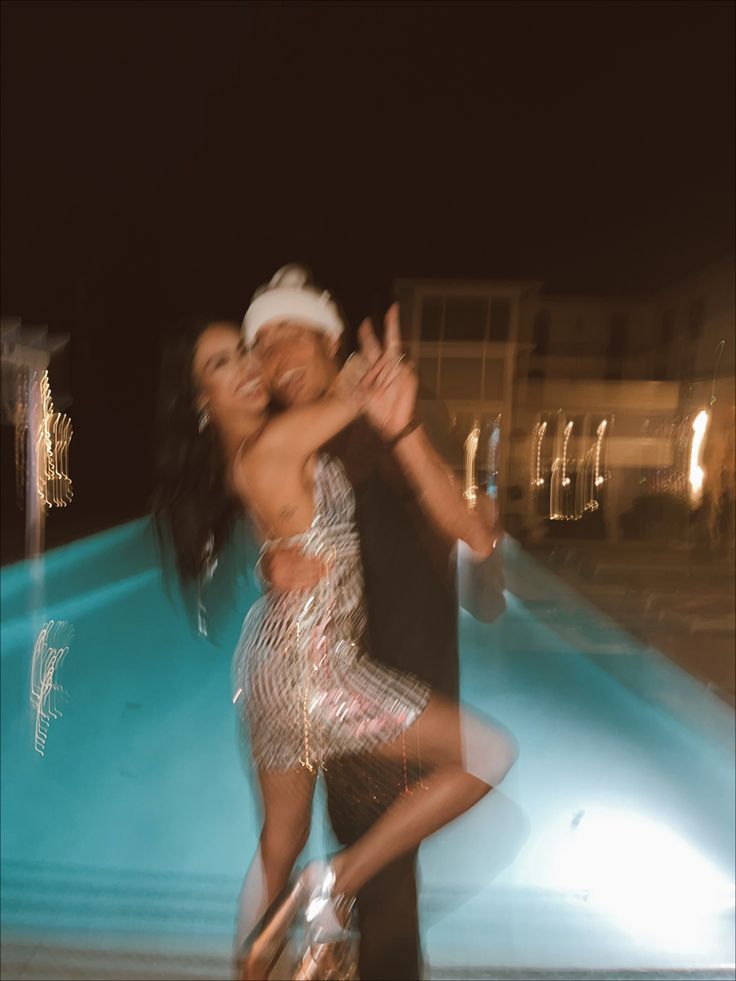 two people are dancing in front of a pool at night with their arms around each other