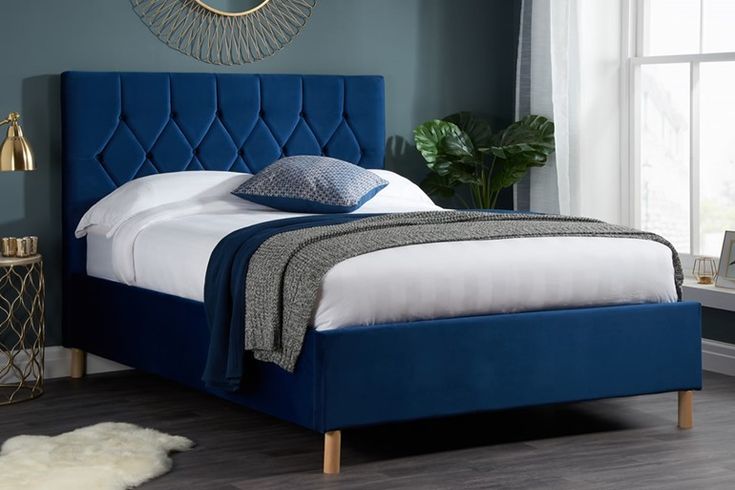 a bed with a blue headboard and white sheets in a room next to a window