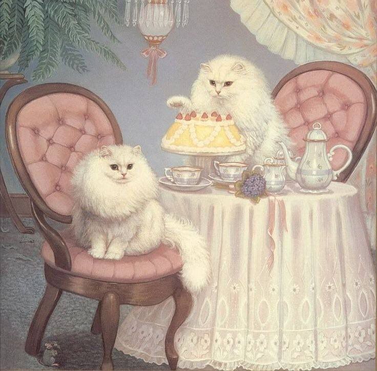 two white cats sitting at a table with a cake and teapot on it, in front of a chandelier