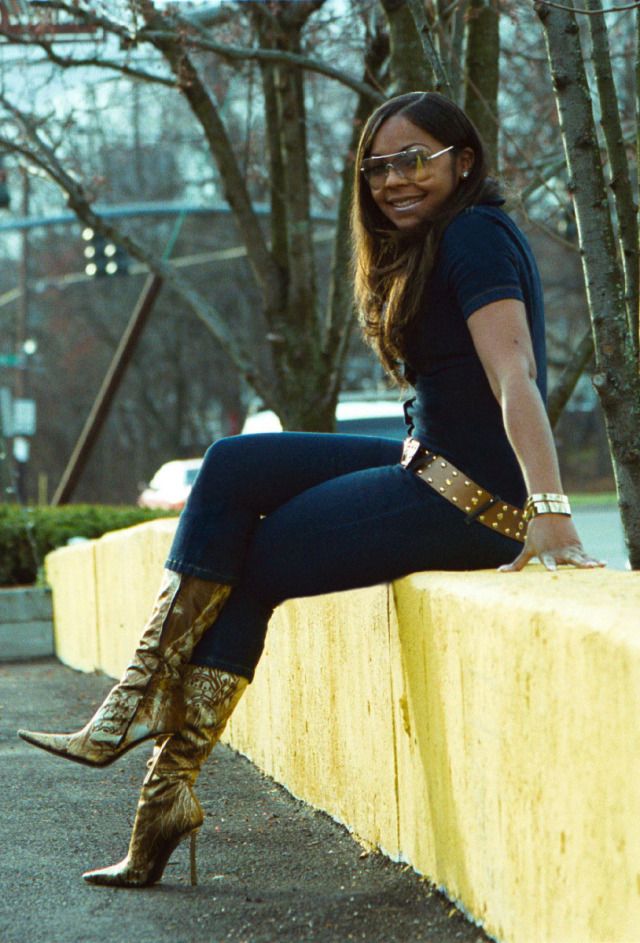 a woman sitting on top of a yellow wall next to a tree and wearing boots