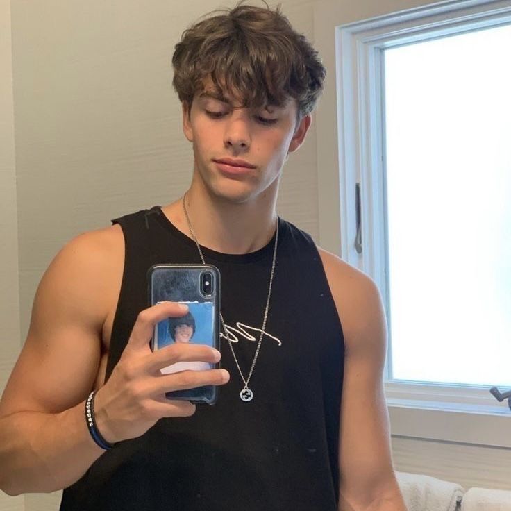 a young man is looking at his cellphone in the mirror while wearing a black tank top