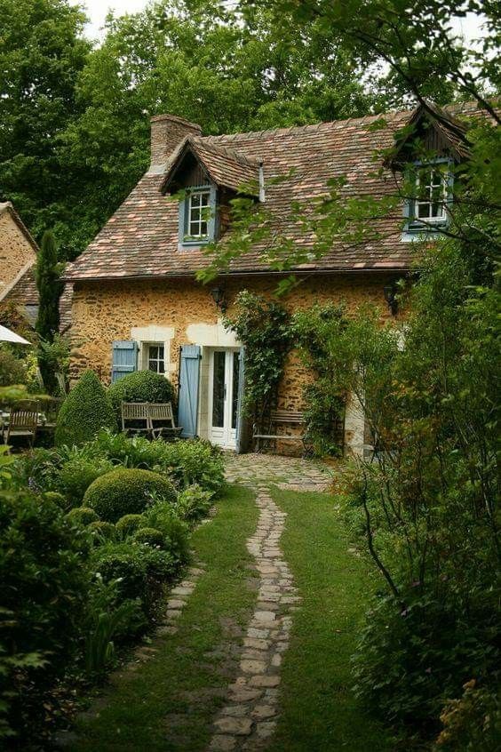 a stone house with blue shutters and windows in the front yard is surrounded by greenery