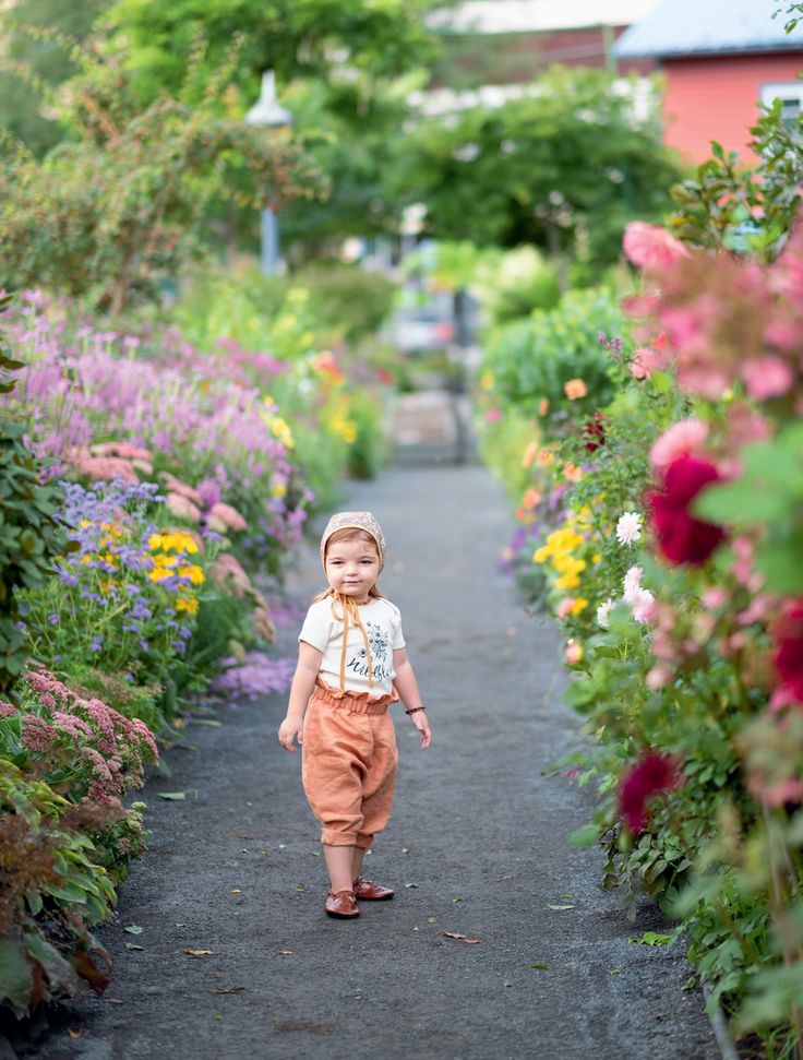 a little boy that is walking down a path with flowers on both sides and trees in the background