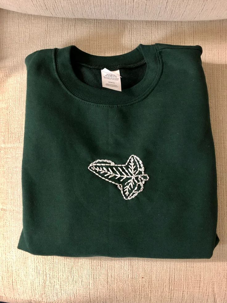 a green sweatshirt with an embroidered leaf on it