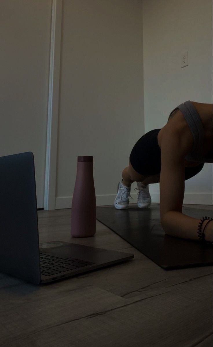 a woman doing push ups in front of a laptop