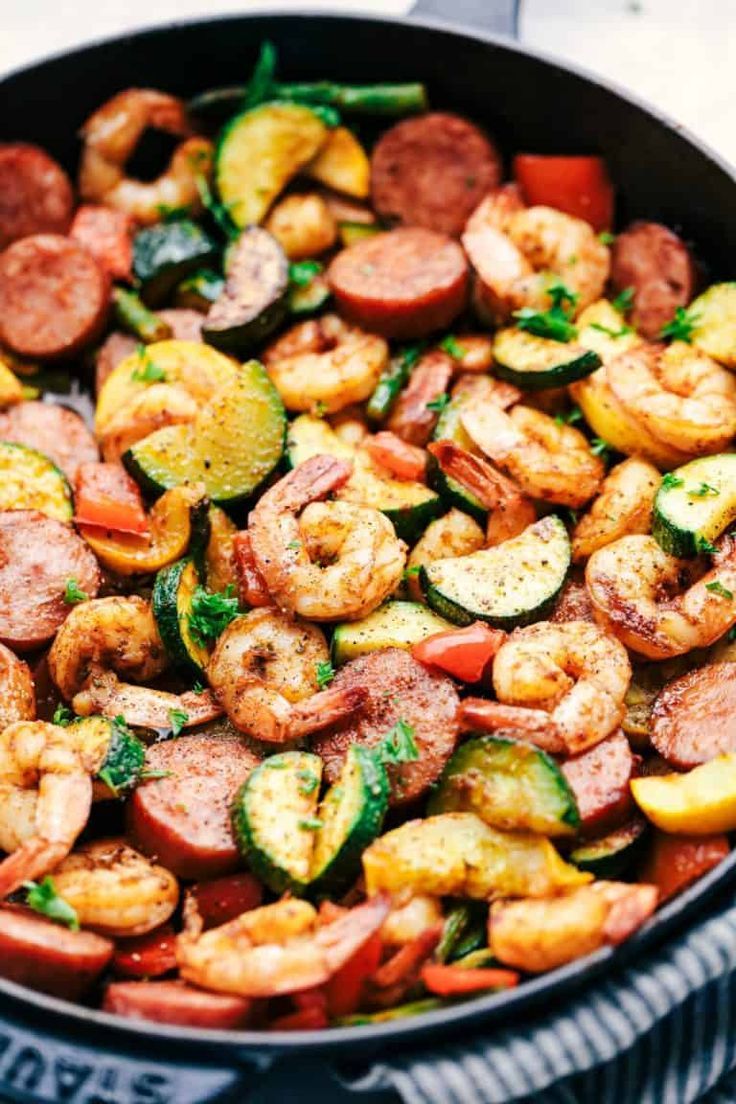 a skillet filled with shrimp, zucchini, and vegetables on top of a table