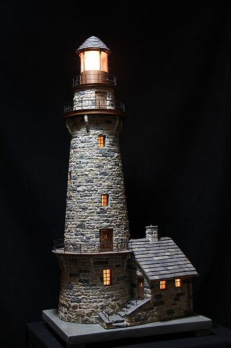 a model lighthouse is lit up on a black background with light coming from the top