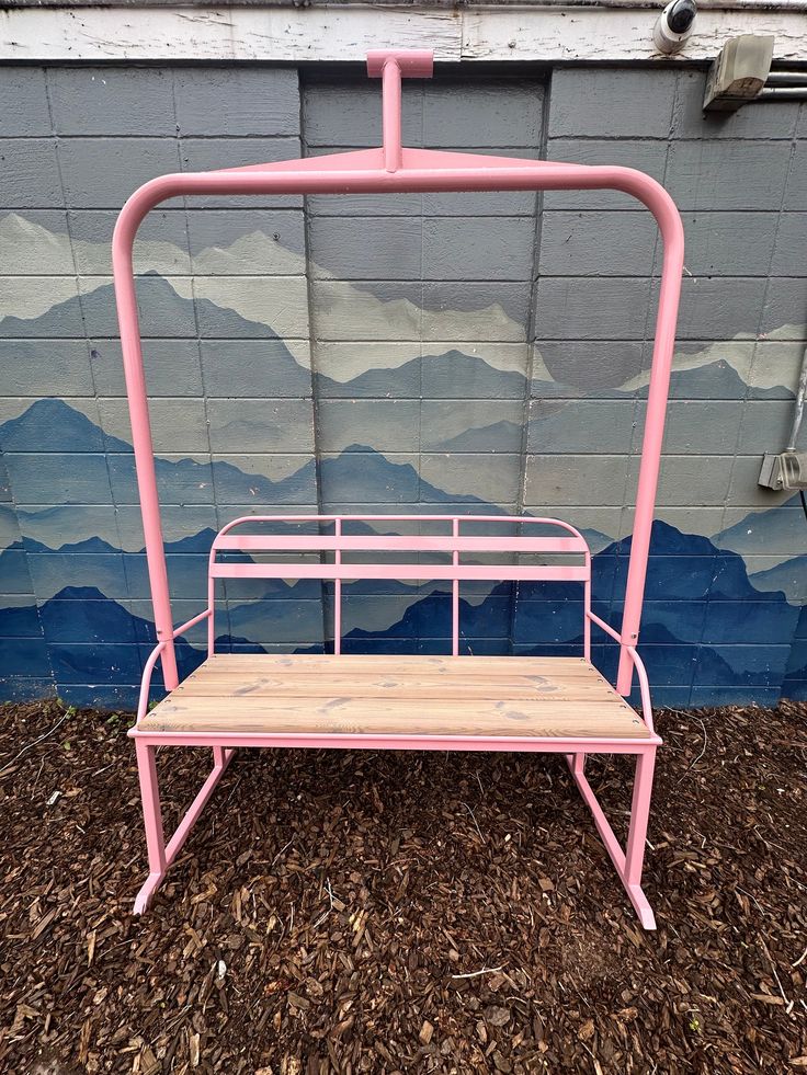 a pink metal bench sitting in front of a wall