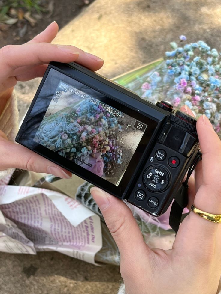 a person holding up a camera to take a photo with flowers on the ground in the background