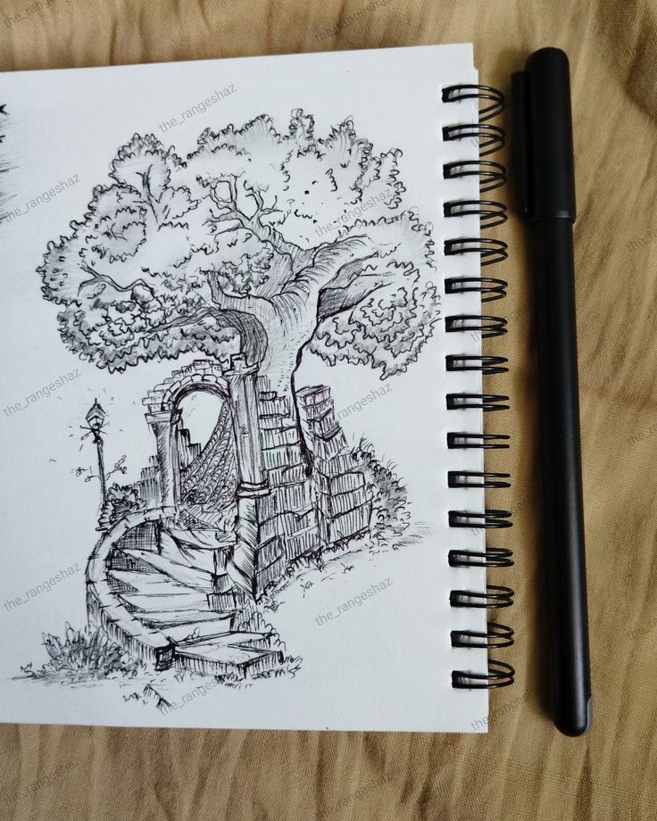 a pen is sitting next to a notebook with a drawing of a tree on it