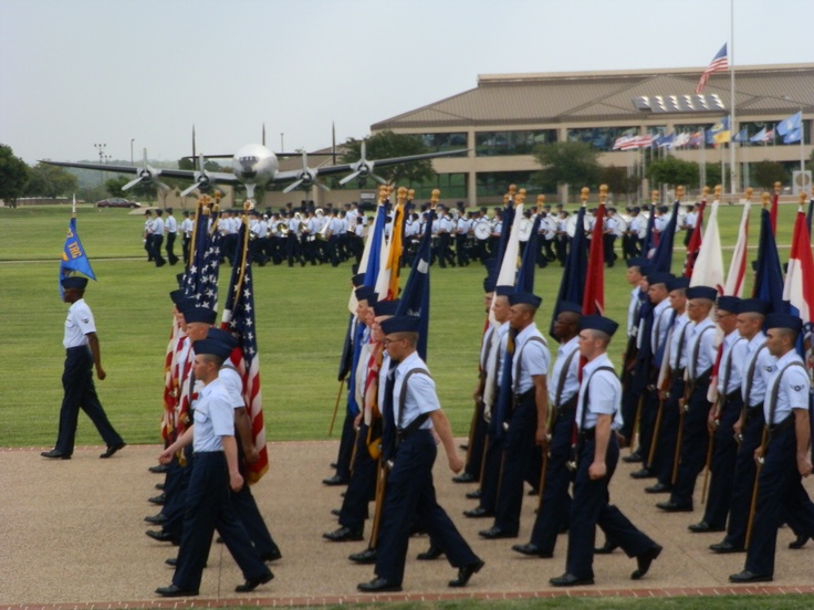 a group of men in uniform walking down a street next to flags and an airplane