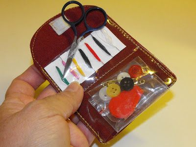 a hand holding a pair of scissors next to a small case with sewing supplies on it