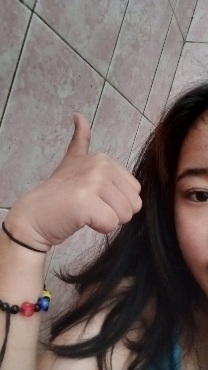 a woman with long hair giving the thumbs up sign while standing in front of a tile floor