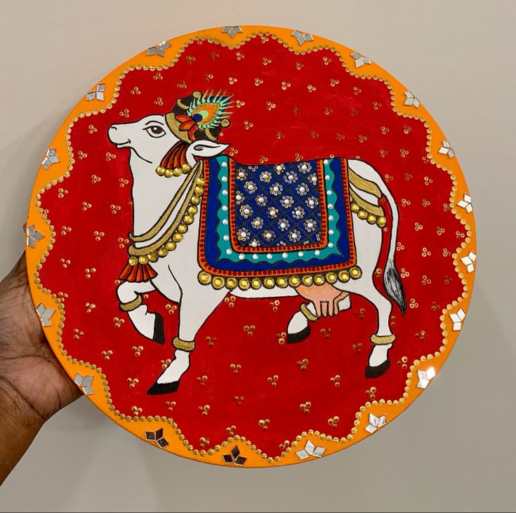 a hand holding a decorative plate with a cow painted on it