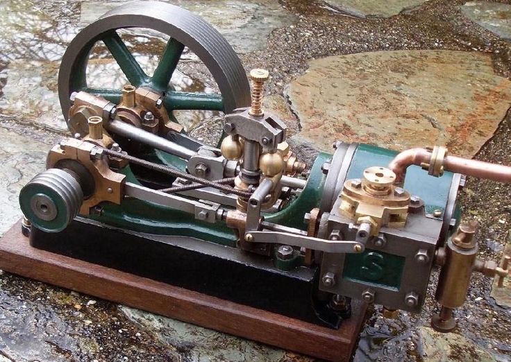 an old fashioned machine is sitting on the ground next to some rocks and stones with water coming out of it