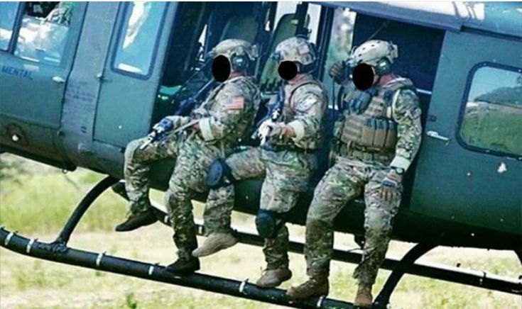 three soldiers sitting on the side of a helicopter with their feet in the air while another man stands next to them