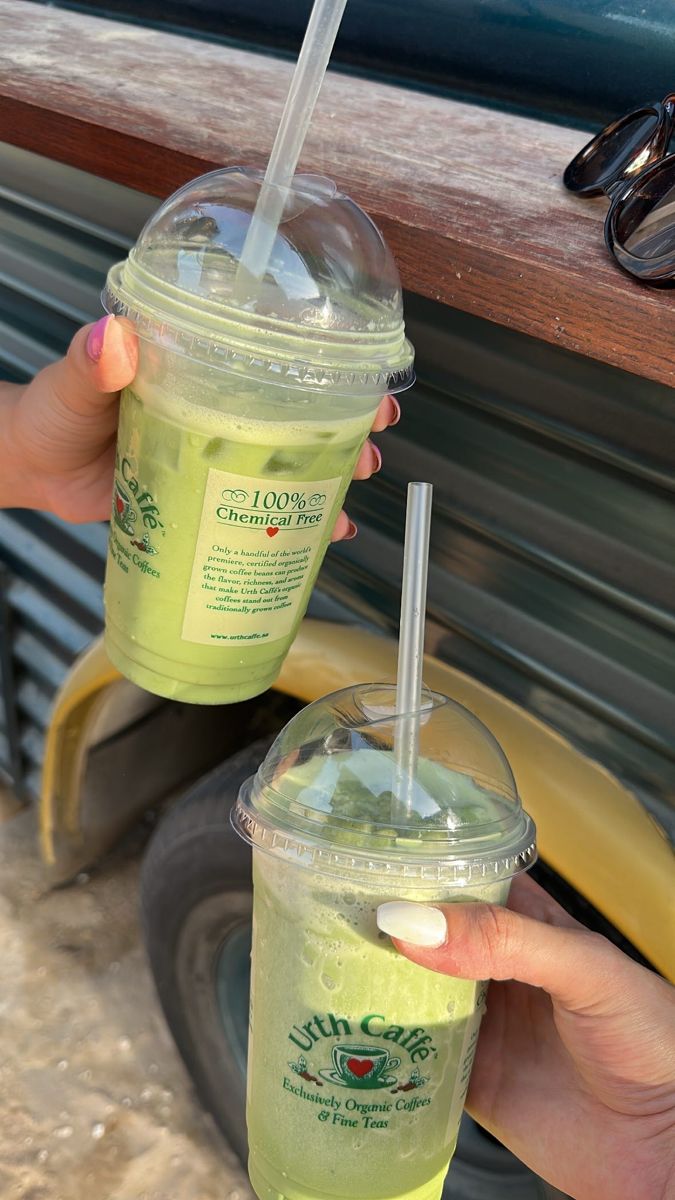 two people holding up drinks in front of a vehicle with their hands on the table