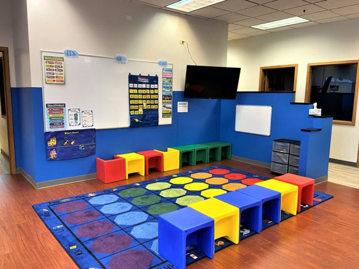 a classroom with blue walls and colorful play mats on the wooden floor, while several children's toys are scattered around