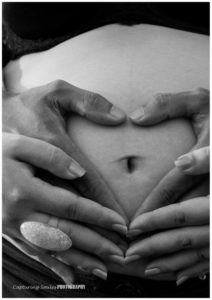 two hands making a heart shape on top of a pregnant woman's belly in black and white