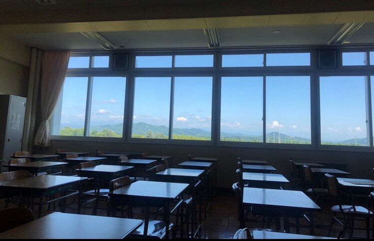 an empty classroom with many desks and windows looking out on the mountain range in the distance