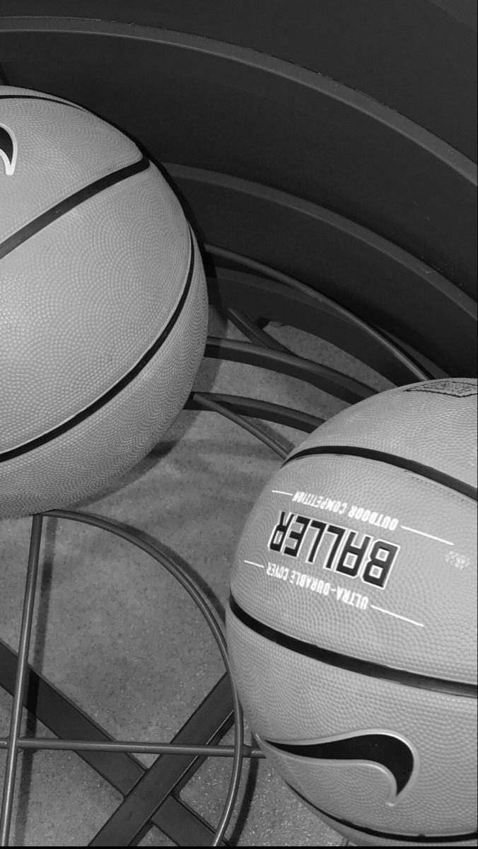 two basketballs sitting on top of each other in front of a metal rack filled with balls