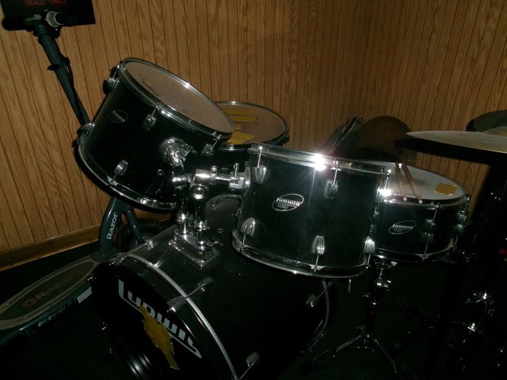 a black drum set sitting on top of a floor next to a wooden paneled wall