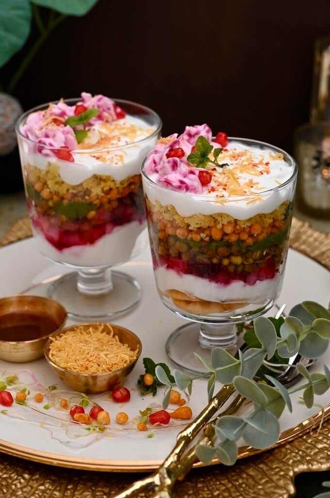 two layered desserts on a plate with flowers and greenery in the background text reads 7 layer dahi chaat