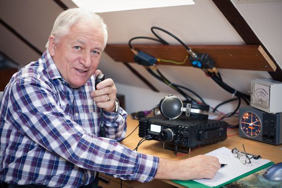 an older man sitting at a desk in front of a camera and some electronic equipment