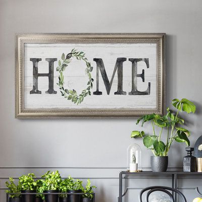 a framed sign that says home with potted plants on the shelf in front of it