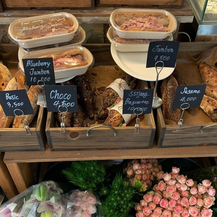 several different types of food on display at a market stall with price signs and flowers