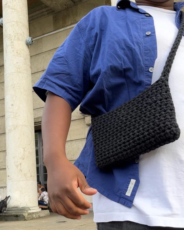 a man holding a crocheted black bag in front of a white building with columns